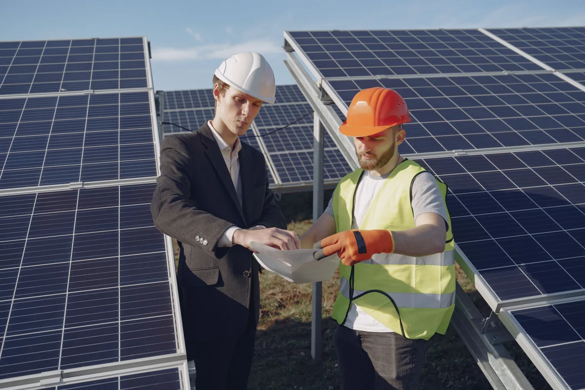 Two professionals reviewing documentation beside solar panels
